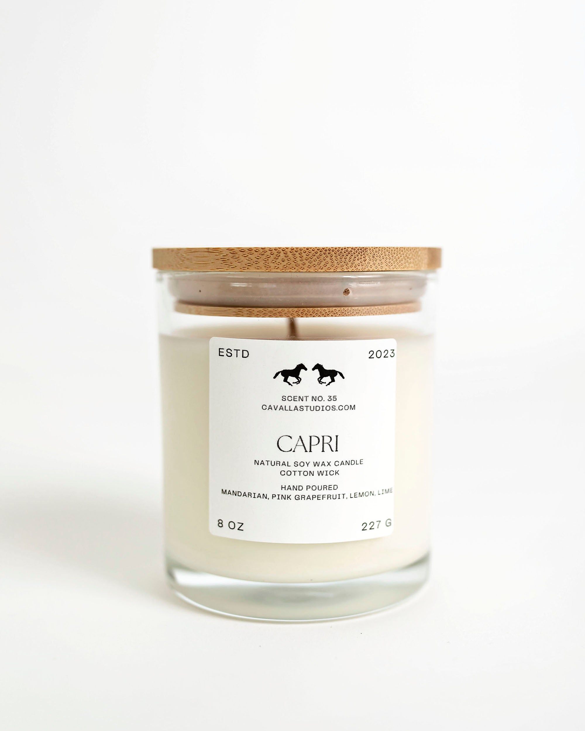 A white soy wax candle in a clear glass vessel with a bamboo lid, labeled 'Capri' with the brand 'Cavalla Studios' and establishment date '2023'.