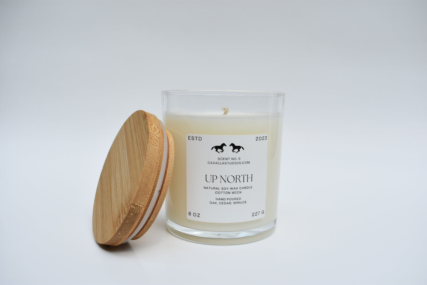 Classic white candle in a clear glass vessel, a bamboo lid leans against the vessel. The glass features the 'Cavalla Studios' logo and the candle is labeled with the scent name 'Up North.'